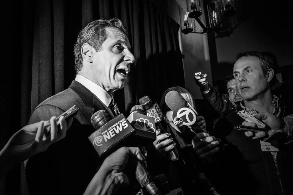 Un homme en costume est entouré de journalistes et de microphones lors d'une conférence de presse.
