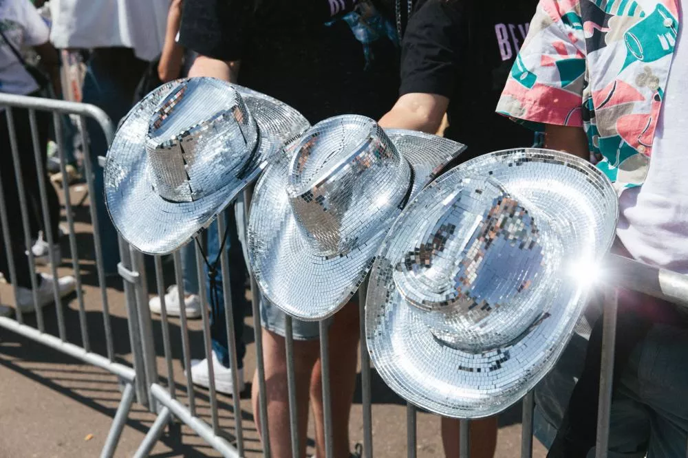 Des personnes tiennent des chapeaux de cowboy recouverts de miroirs, semblables à des boules à facettes, derrière une barrière.